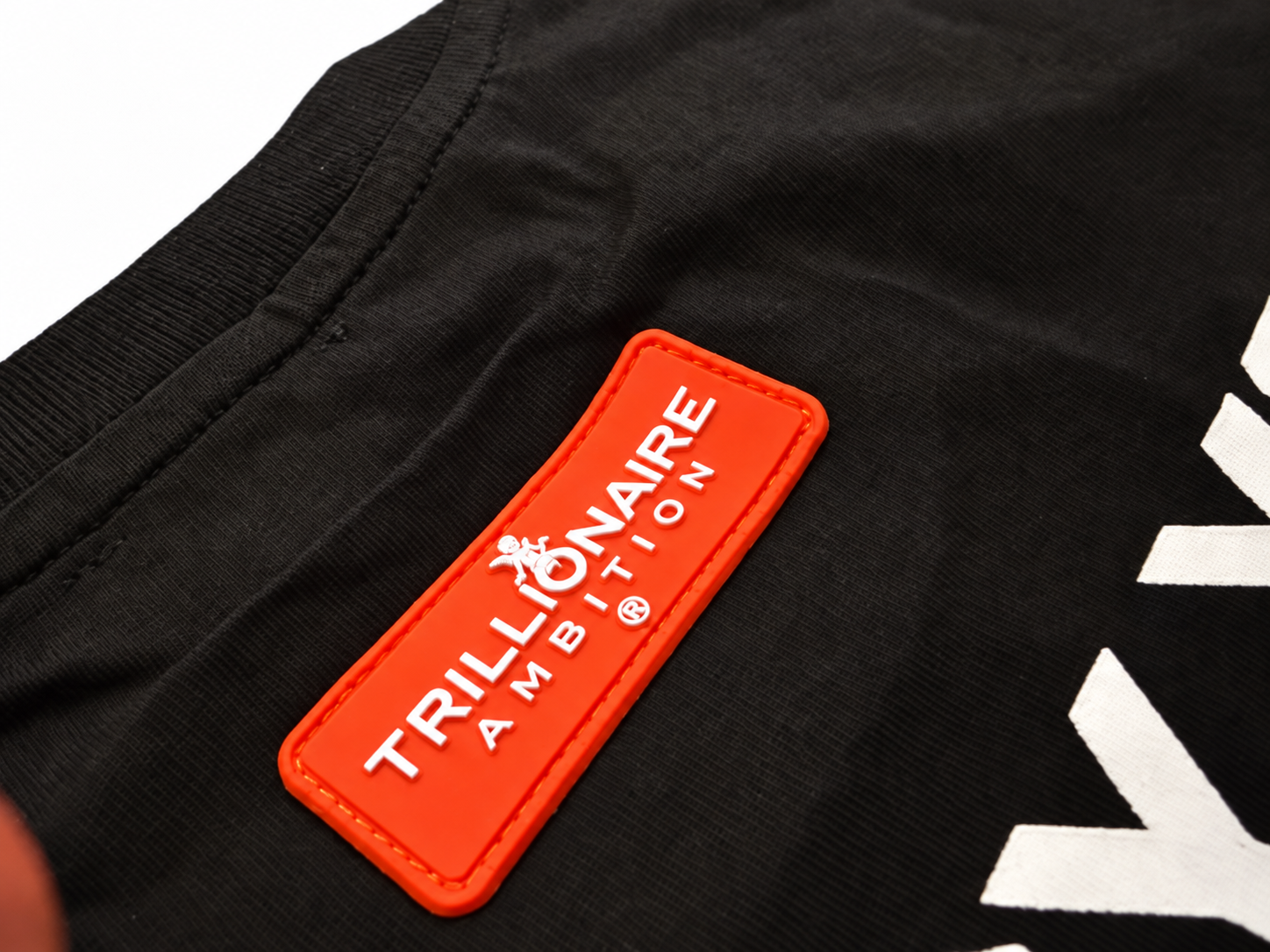 Close-up of the orange-red rubber patch with the Trillionaire Ambition wordmark raised in white